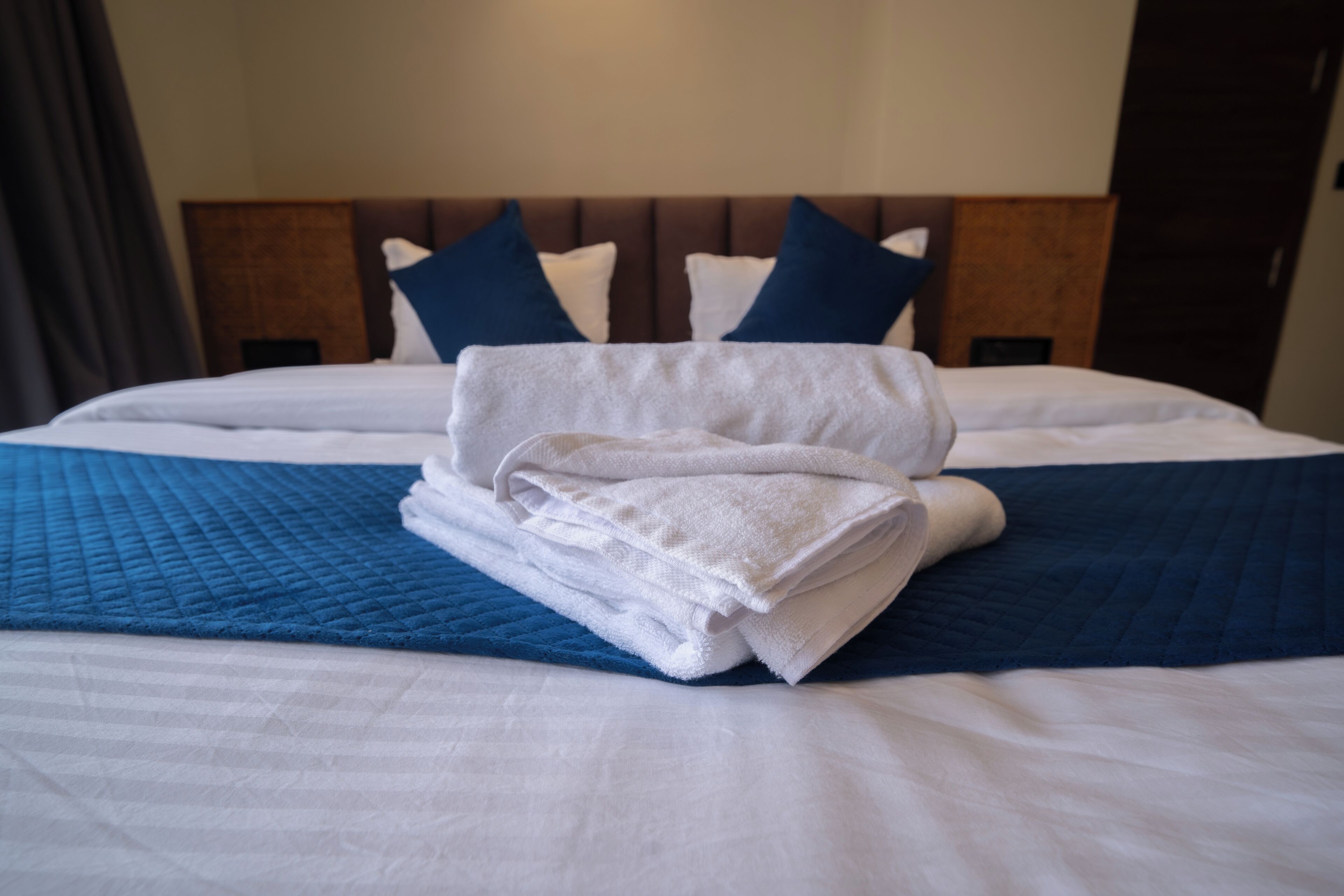 A neatly made bed with a blue quilt, white linens, and folded towels.