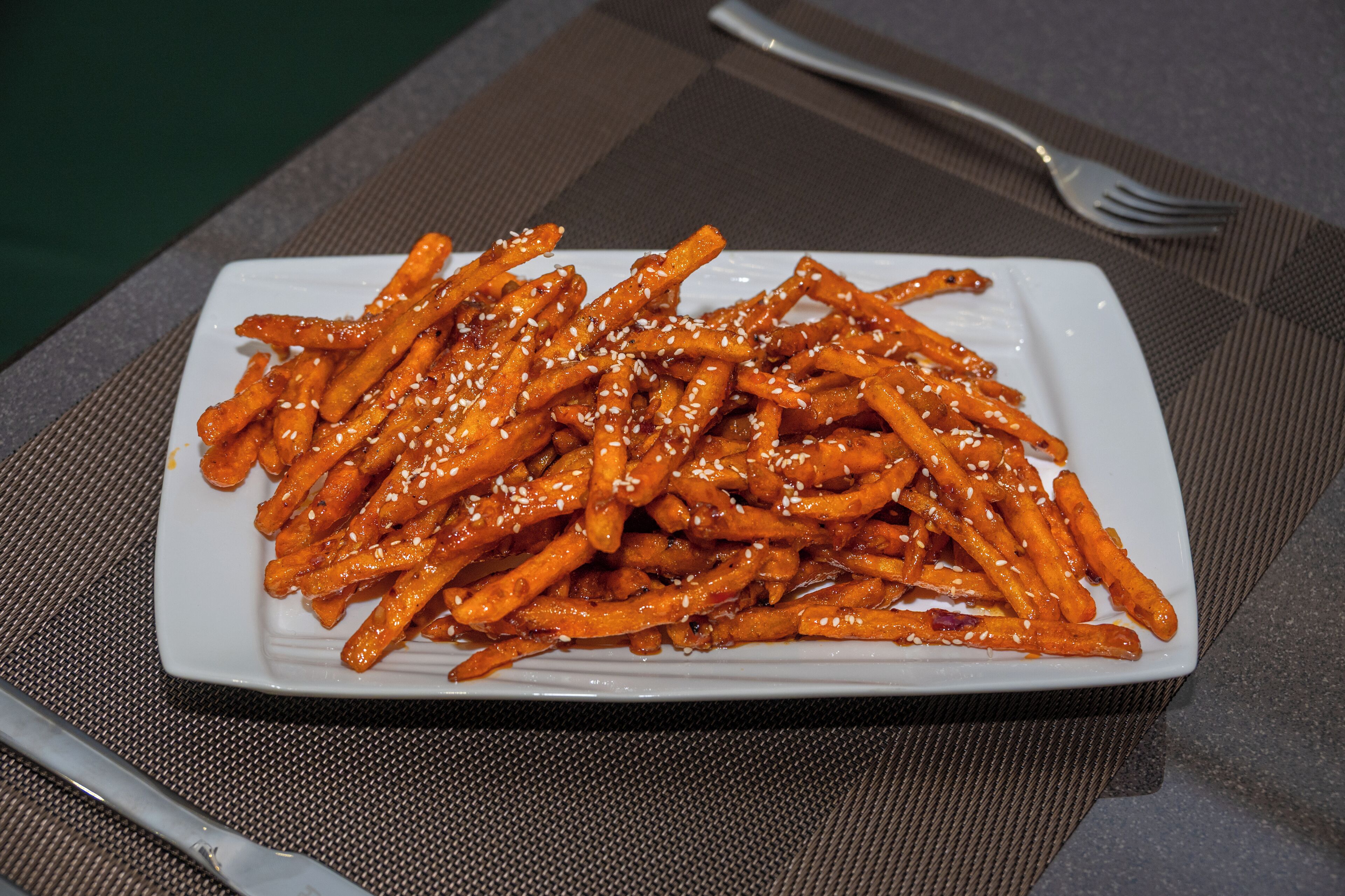 A white rectangular plate of food with sesame seeds on a textured placemat.