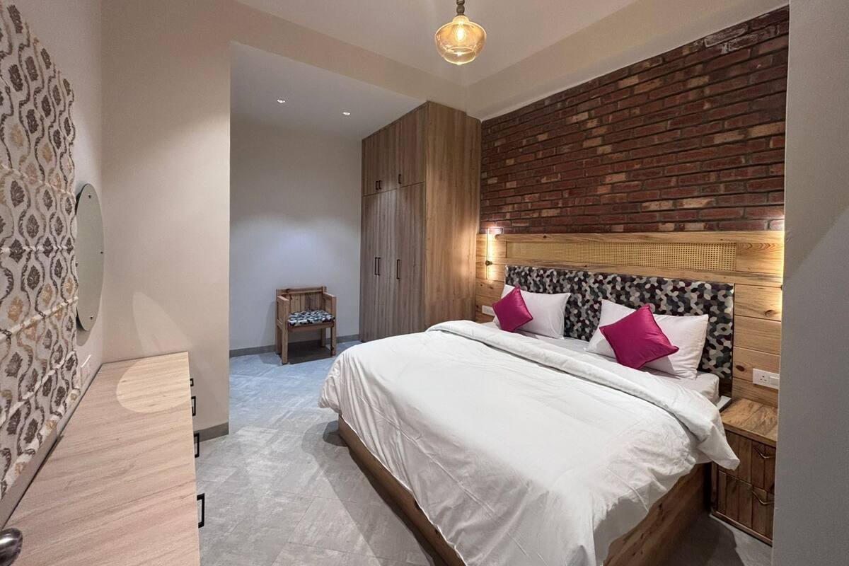 Une chambre moderne avec un grand lit, une tête de lit en bois et un mur d’accent en briques.