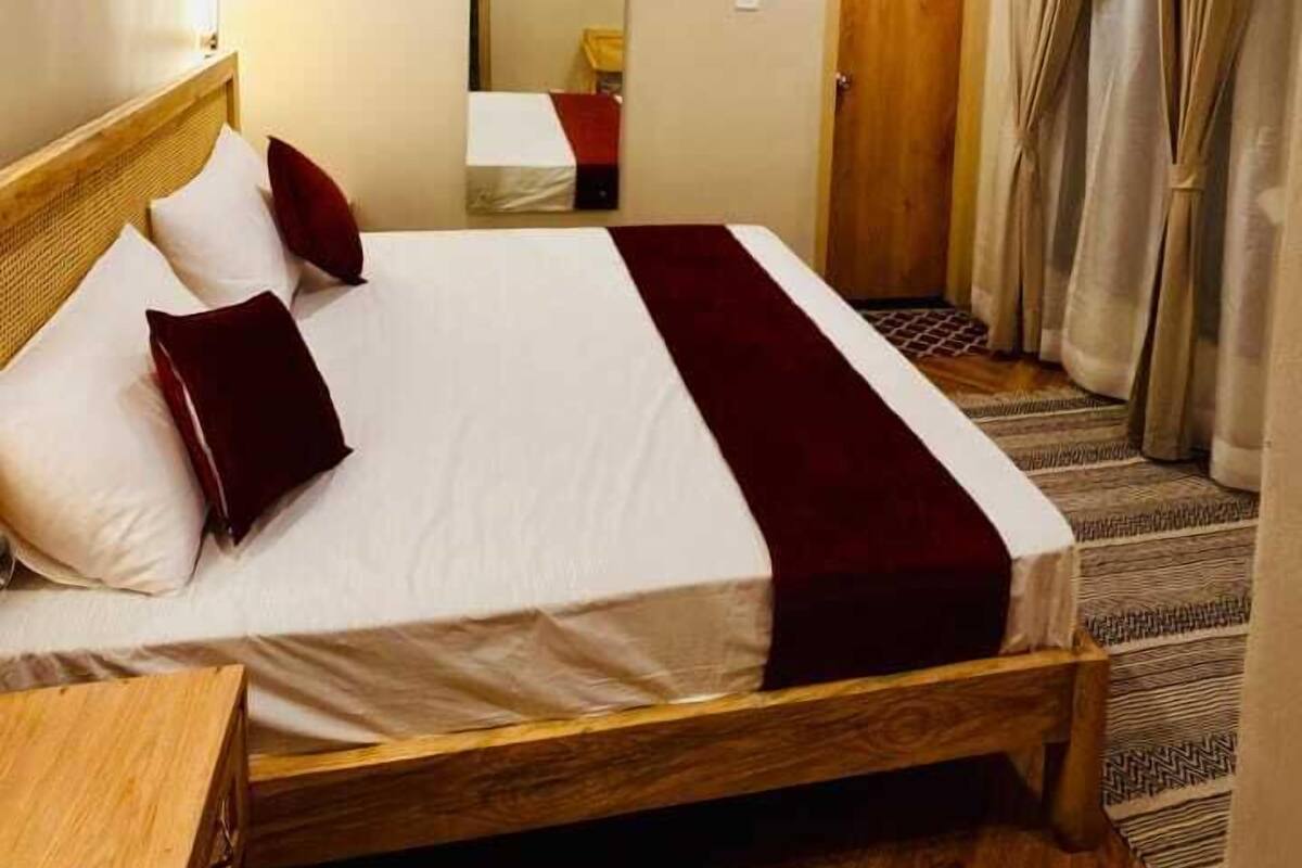 Une chambre d’hôtel avec un lit en bois, une table de chevet, un miroir et une porte avec des rideaux.