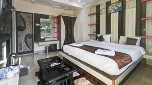 A modern bedroom with a large bed, a coffee table, a TV, and a wardrobe. - Suketi Stays (Mahabaleshwar)