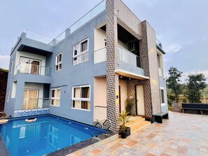 A modern two-story house with a swimming pool, balconies, and a stone facade. - Suketi Stays (Mahabaleshwar)