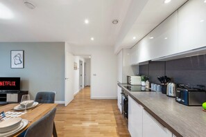 A modern kitchen with a wooden countertop, built-in appliances, and a dining area with a table set for two. - Cozy 2BR Wembley | Sleeps 5 | Near Train | Prime (London)