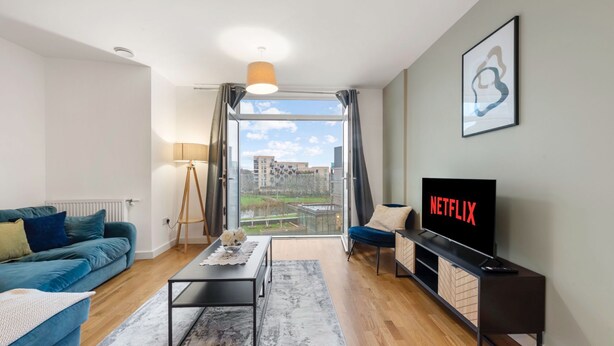 Una sala moderna con sofá, mesa de centro, televisor y vistas a través de un ventanal amplio.