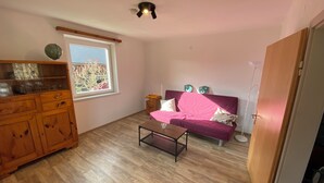 Quarto com armário de madeira, sofá rosa, mesa pequena e janela com vista para árvores.