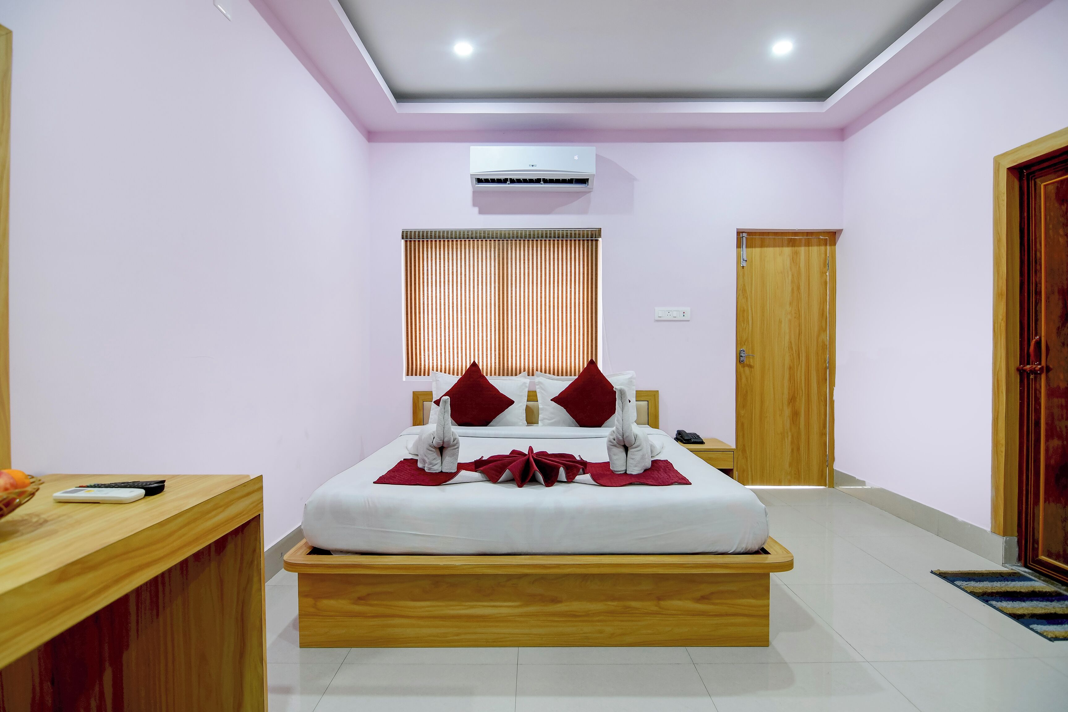 A hotel room with a bed, bedside table, wooden floor, and an air conditioning unit.