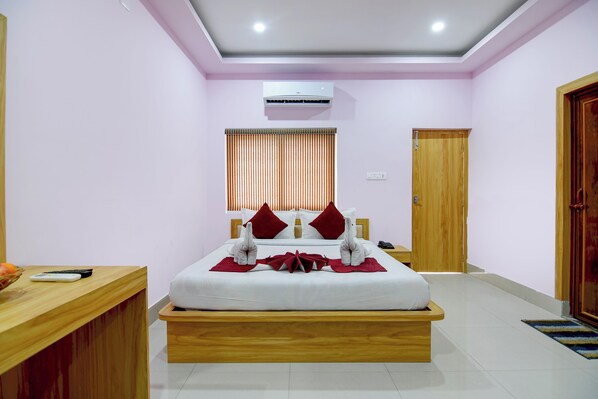 A hotel room with a bed, bedside table, wooden floor, and an air conditioning unit. - Hotel Chaitrangada (Bolpur)