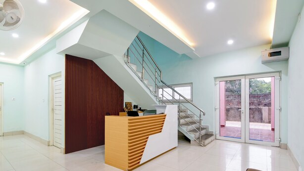 A reception area with a wooden desk, a staircase, and a glass door leading outside. - Hotel Chaitrangada (Bolpur)
