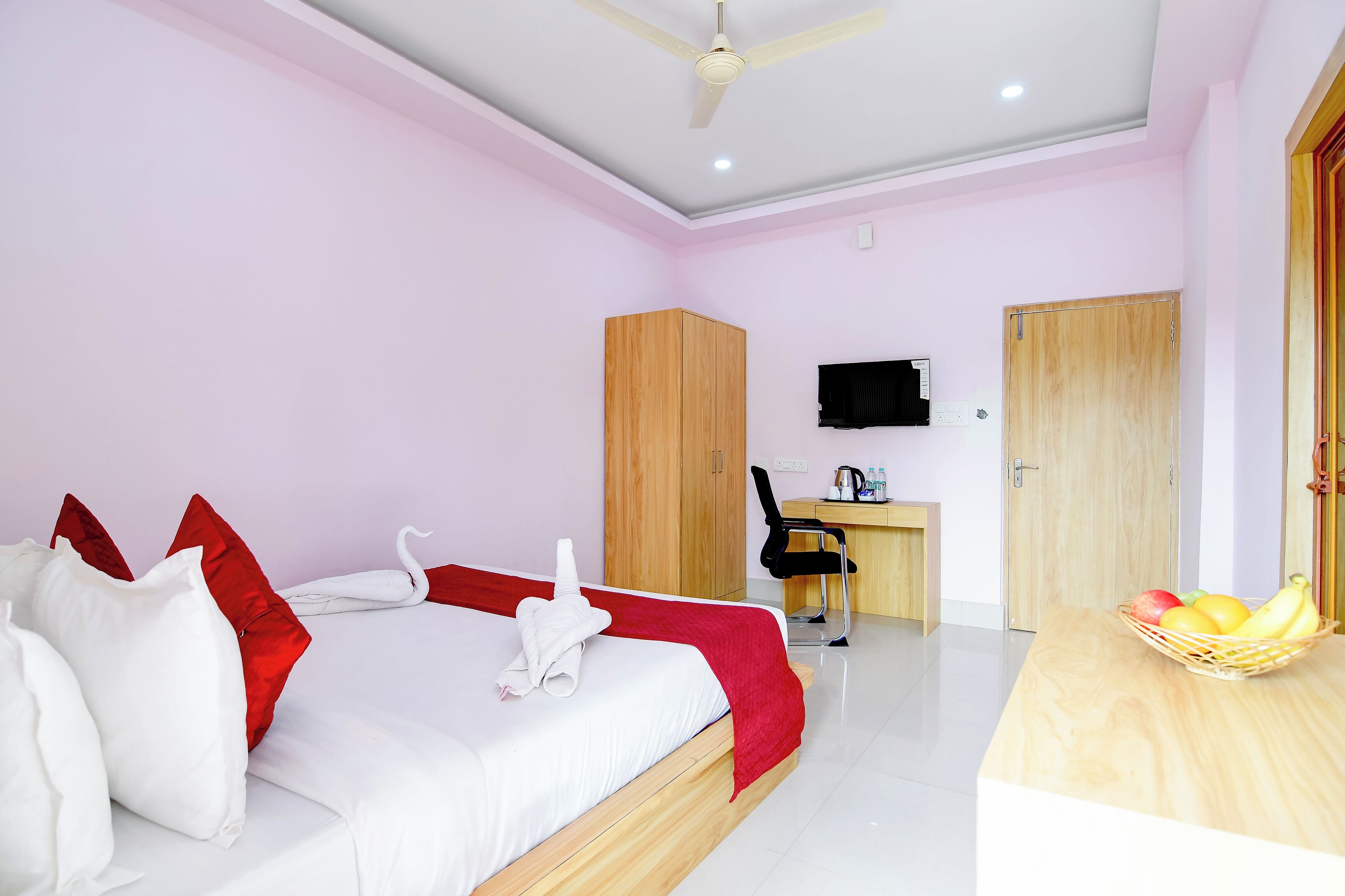 A hotel room with a bed, a desk, a chair, a television, and a fruit basket.