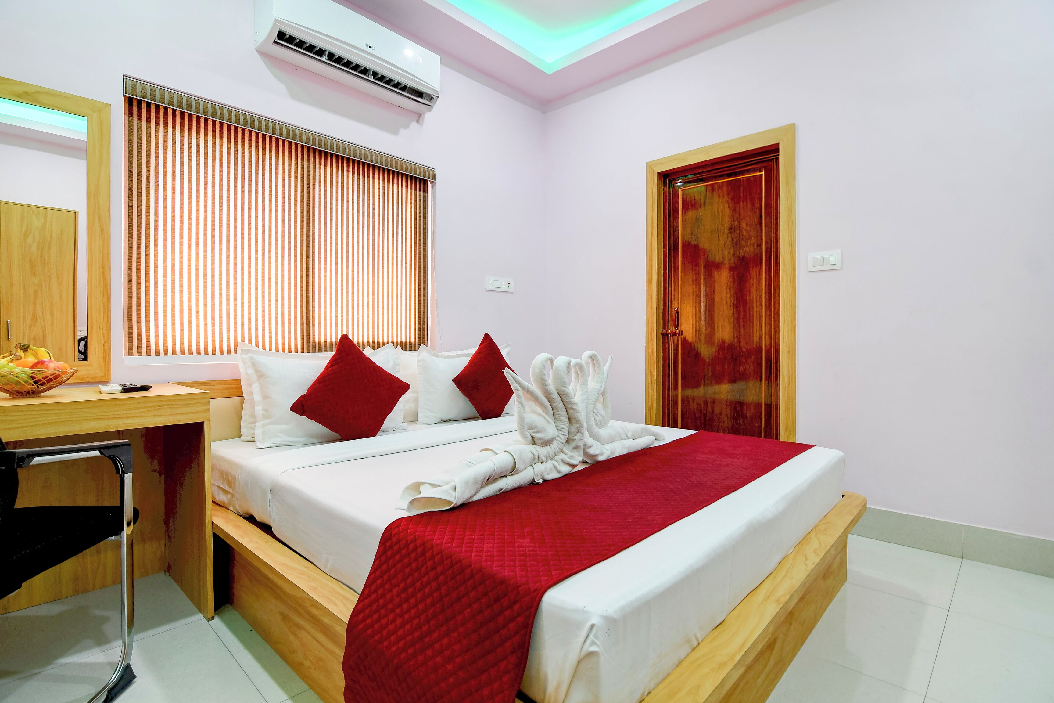 Habitación de hotel con cama, escritorio, silla, ventana con persianas y unidad de aire acondicionado.
