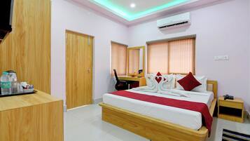 Una habitación de hotel con una cama de madera, un escritorio, una silla, aire acondicionado y una zona de recepción con mostrador y algunos objetos encima.