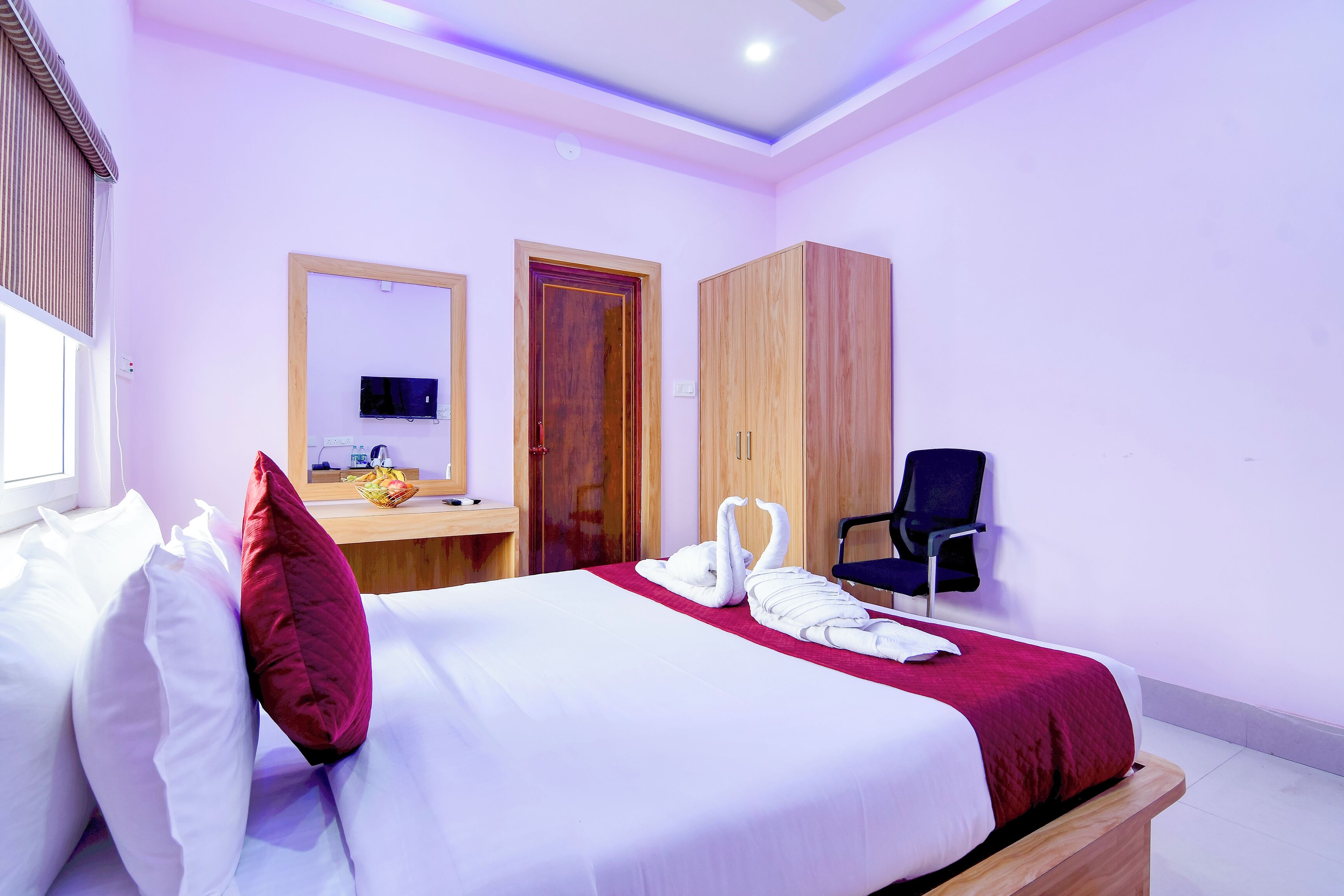 Quarto de hotel com cama, escrivaninha, cadeira, televisão e guarda-roupa.
