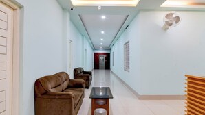 A hallway with a sofa, a small table, and a standing fan. - Hotel Chaitrangada (Bolpur)