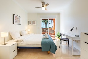A bedroom with a bed, bedside tables, a desk, and a chair. There is a ceiling fan, a window, and a door leading to a balcony. - Resort Mediterra III | Modern Apartment with Sea & Mountain Views, Terrace & Pools in Benalmadena (Benalmádena)