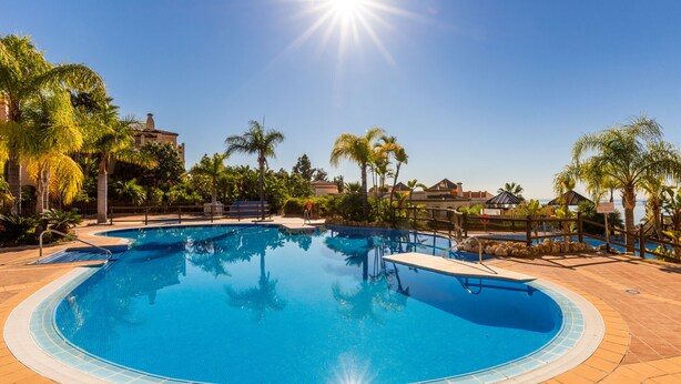 A large, clear swimming pool surrounded by palm trees and a tiled deck. - Resort Mediterra | Sea View Apartment near Golf with Pools & Fitness (Benalmádena)