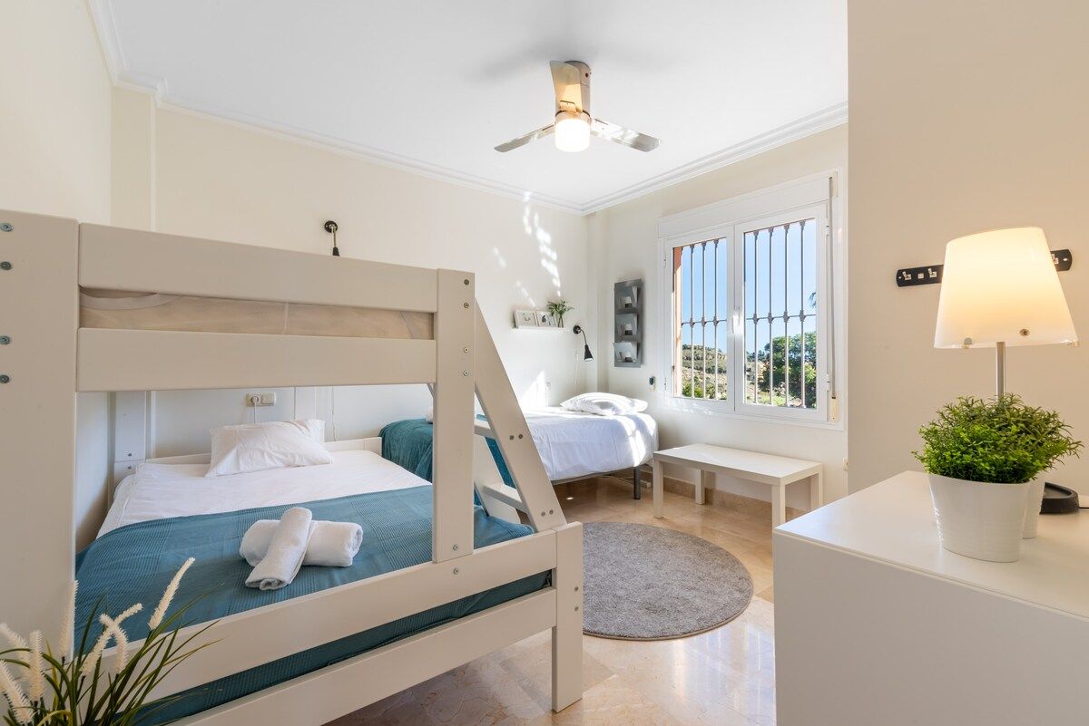 Une chambre avec un lit superposé, un bureau, une chaise, une lampe et une fenêtre donnant sur un beau paysage.