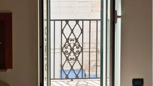 An open door leading to a balcony with a metal railing and a view of a building with a blue window. - Dimora GiuLè - Arcuève (Ostuni)
