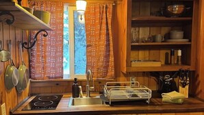 Una cocina compacta con paredes de madera, estufa empotrada, un lavabo y una ventana con cortinas.