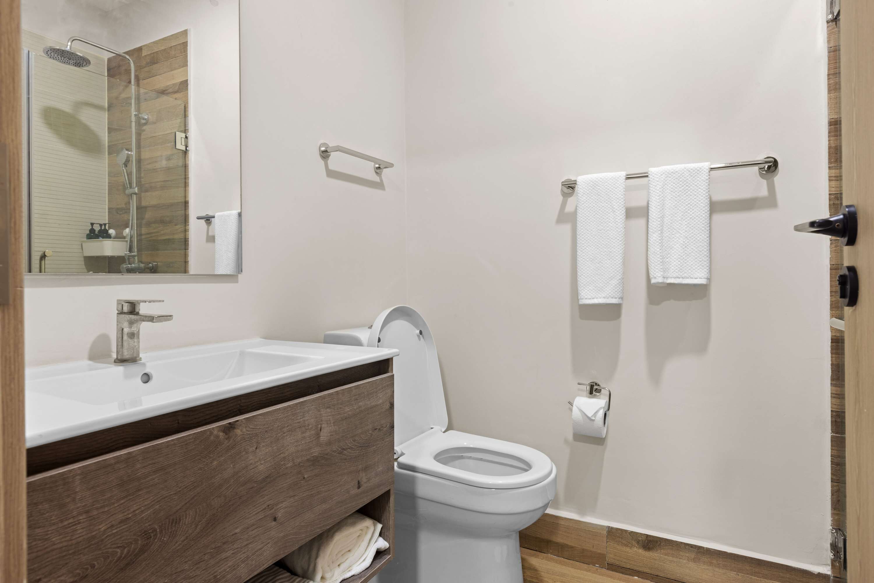A modern bathroom with a wooden vanity, a white sink, a toilet, and a towel rack.