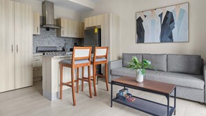A modern kitchen with wooden cabinets, a built-in stove, and a grey sofa in the living area. - NOK Modern 1BR Apartment With Terrace in Vistacana (Punta Cana)