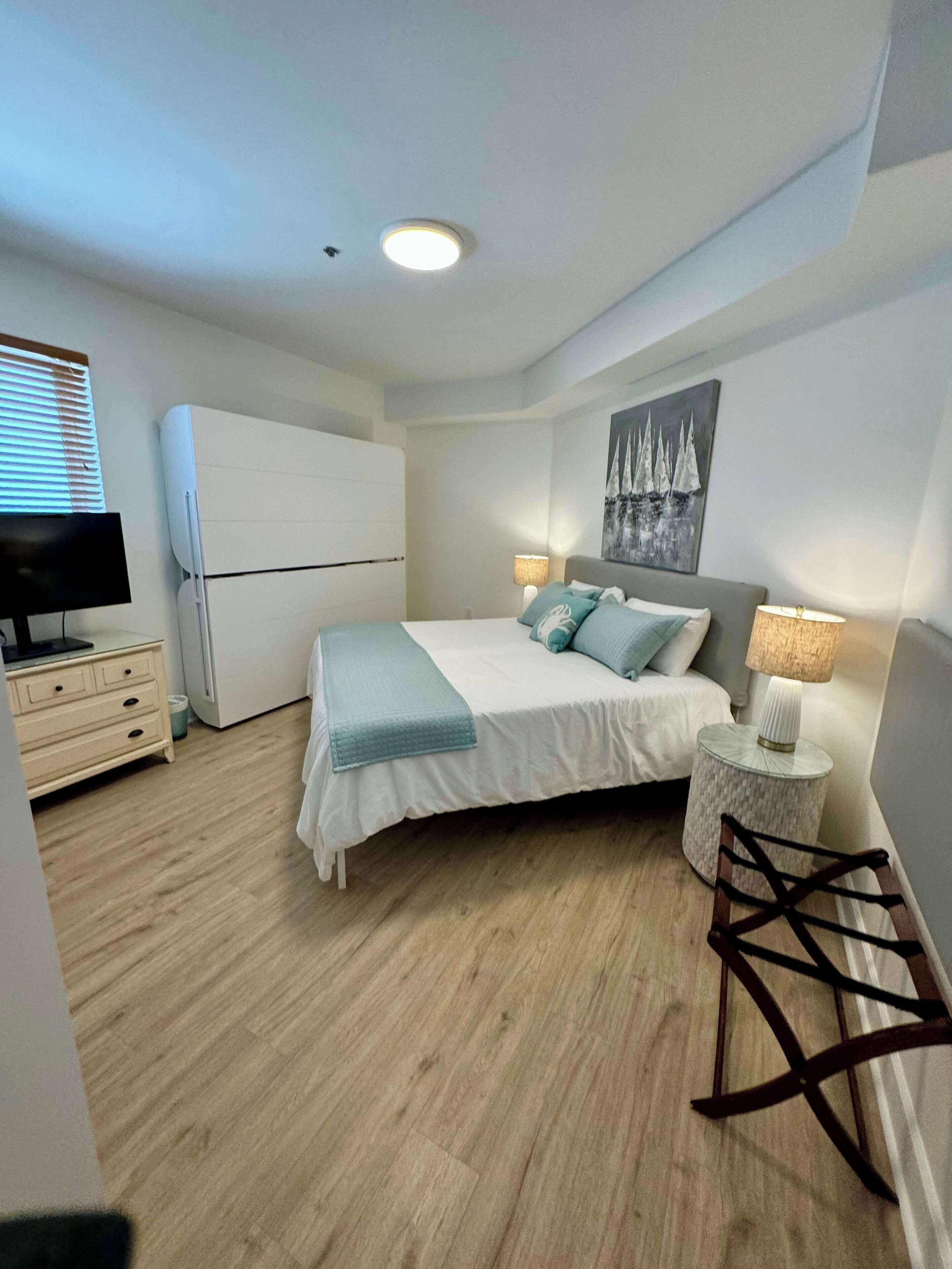 Une chambre à coucher avec un lit, des lampes de chevet, une télévision, une armoire et un tableau au mur.