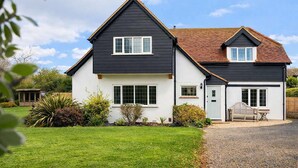 A two-story house with a dark exterior and white trim, a front porch, and a well-maintained lawn. - Spacious Coastal Family Home Sleeps 8 (Bognor Regis)