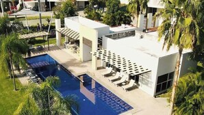 A pool area with lounge chairs and umbrellas, surrounded by palm trees and a modern building. - Casa Nido de Mar 9 Persons Occupancy Pool 7 Beds (Nuevo Nayarit)