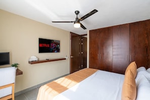Un dormitorio con cama, televisor montado en la pared, ventilador de techo y armario de madera.