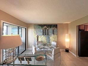 A modern kitchen with a glass dining table, white chairs, a refrigerator, and a wall with abstract art. - CQS 46 Veronese CT Conquistador (St. Augustine)