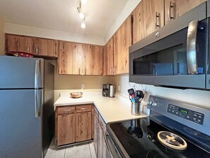 A modern kitchen with wooden cabinets, a stainless steel refrigerator, a microwave, and a black stove. - CQS 46 Veronese CT Conquistador (St. Augustine)