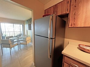 A kitchen with a stainless steel refrigerator, wooden cabinets, a dining table with chairs, and a view through a window. - CQS 46 Veronese CT Conquistador (St. Augustine)