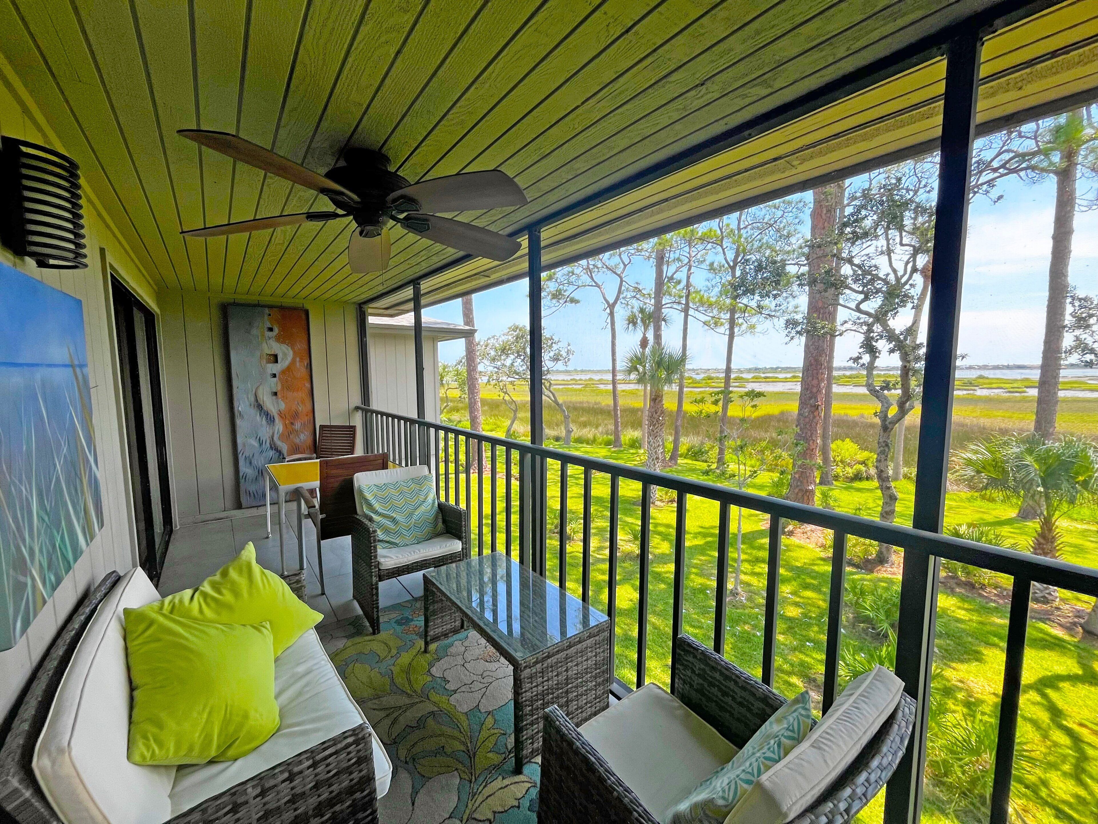 A balcony with wicker furniture, a ceiling fan, and a view of a coastal landscape.