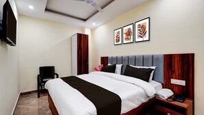 A hotel room with a bed, bedside table, chair, artwork, and a ceiling fan. - Classic Survey Chowk Dehradun (Dehradun)