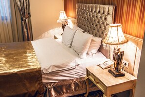 Una cama bien hecha con sábanas blancas, un cabecero capitonado, dos lámparas de noche y un teléfono sobre una mesita de madera.