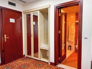 Un pasillo con piso estampado, una puerta de madera con espejo y una puerta roja con un pequeño letrero.