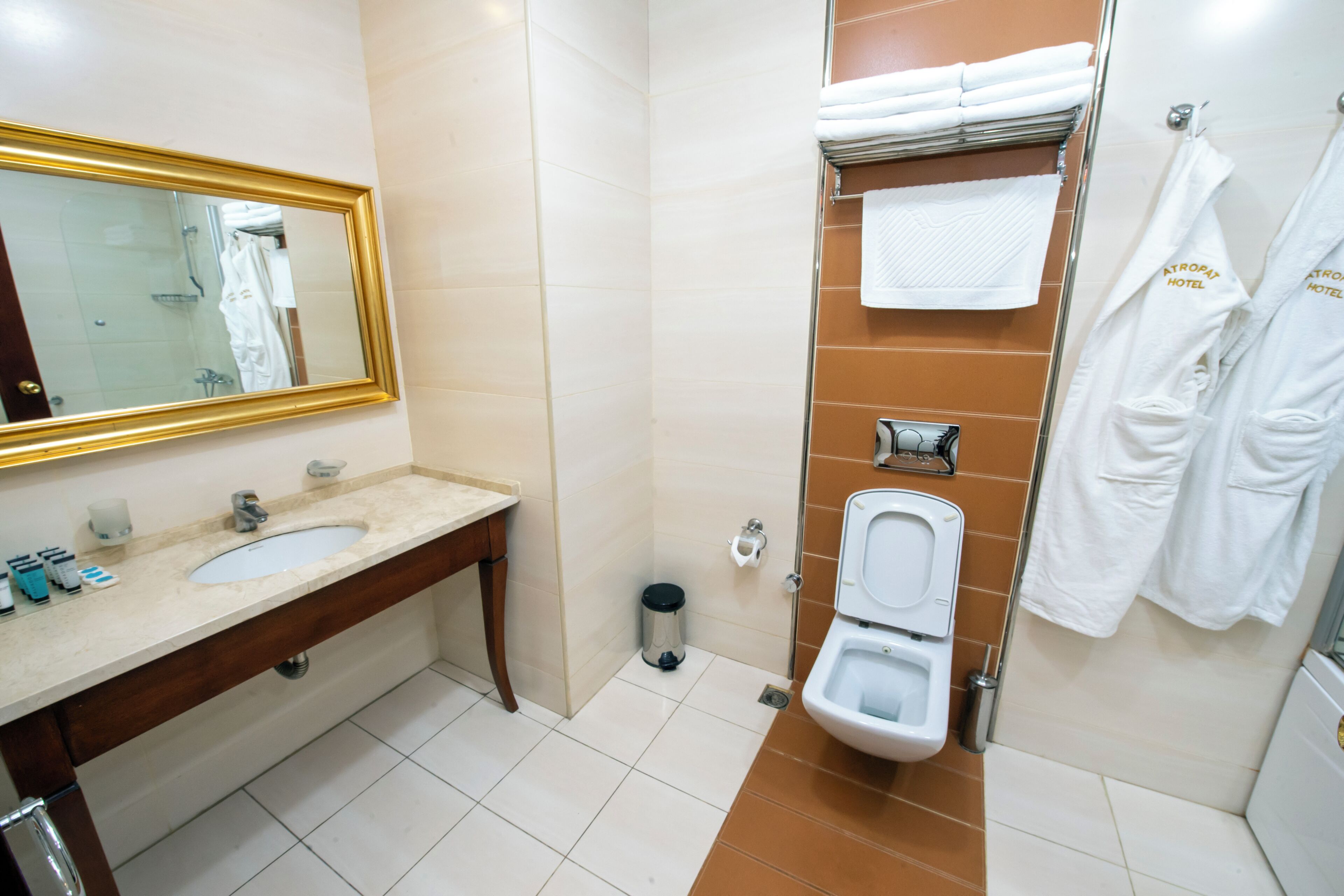 Un baño con lavabo, espejo, inodoro y perchero para toallas.