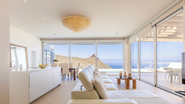 A modern living room with a large sofa, a dining area, and a view of the sea. - Villa Navarra Sunset Adeje (Costa Adeje)