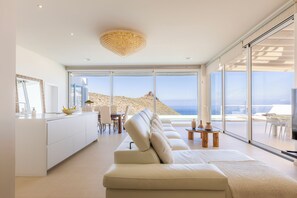 A modern living room with a large sofa, a dining area, and a view of the sea. - Villa Navarra Sunset Adeje (Costa Adeje)