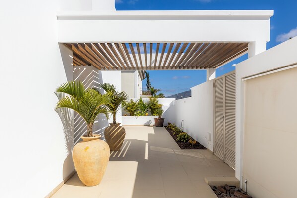 A modern outdoor patio with a wooden pergola, potted plants, and a white wall. - Villa Navarra Sunset Adeje (Costa Adeje)