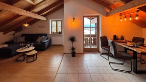 Um quarto de sótão acolhedor, com teto de madeira, área de jantar com mesa e cadeiras, um sofá e uma pequena mesa de centro.