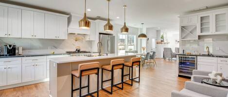 A modern kitchen with white cabinets, a central island with bar stools, and pendant lighting.