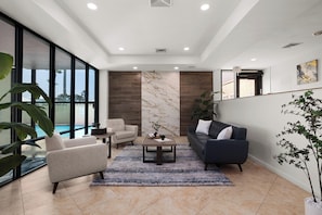 A modern living room with a sofa, armchair, coffee table, and a view of a swimming pool through large windows. - Updated 3BR w/ Gulf Views: Suntide III - Unit 801 (South Padre Island)