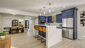 A modern kitchen with blue cabinets, a white island, and bar stools. - Home Theater + Rooftop Deck! Fountain Sq Stunner (Indianapolis)