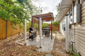 Een achtertuin met een houten pergola, een barbecue en een tafel met stoelen.