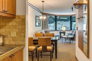 A modern interior with a kitchen, dining area, and seating by a large window. - 1BR Suite w/ Fireplace, Resort Pools, Spa & Gym (Olympic Valley)