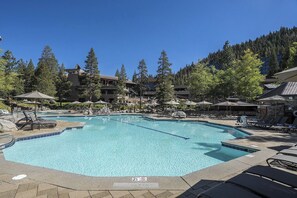 A large outdoor swimming pool surrounded by lounge chairs and umbrellas, with a forested hillside in the background. - 1BR Suite w/ Fireplace, Resort Pools, Spa & Gym (Olympic Valley)