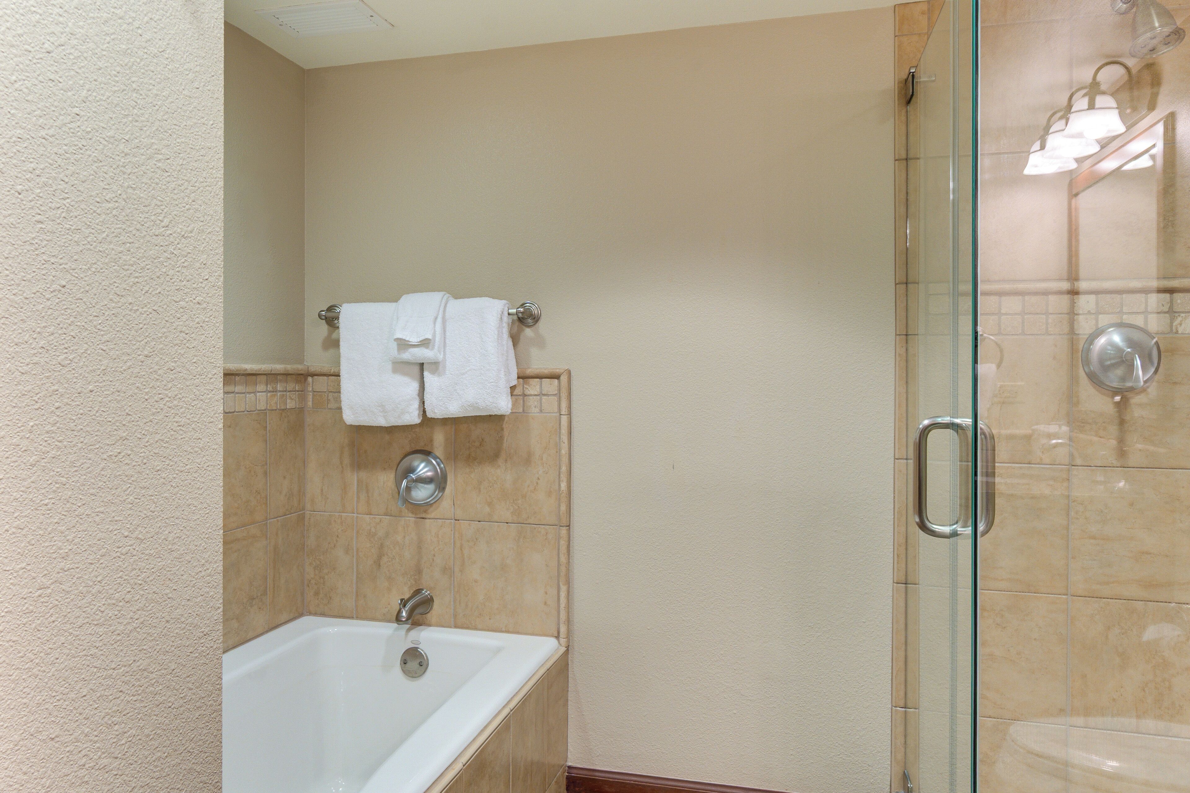 Un baño con bañera, cabina de ducha de vidrio y un perchero con dos toallas blancas.