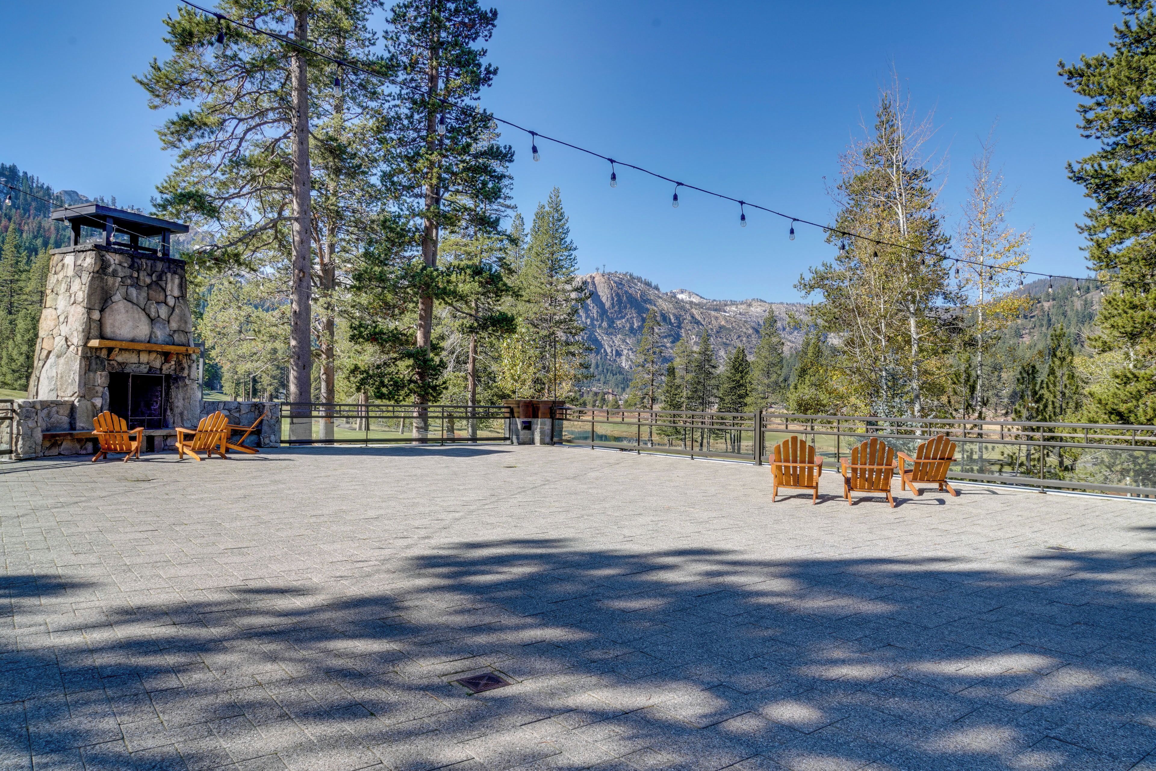Une structure en pierre dotée d’une terrasse en bois et de chaises Adirondack, entourée d’arbres et avec une montagne en toile de fond.