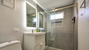 Une salle de bain moderne avec une douche à parois de verre, un lavabo blanc et un grand miroir.