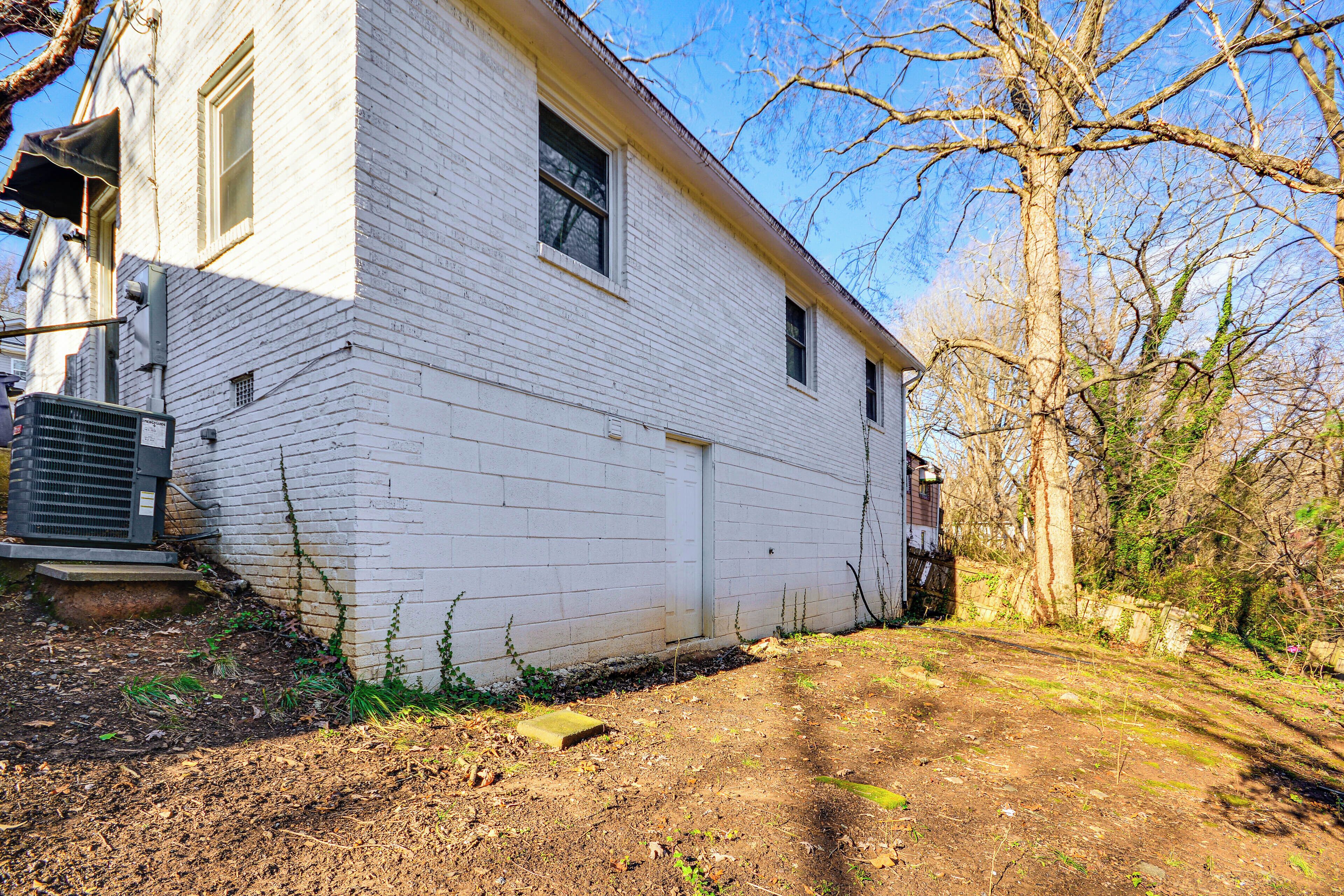 A white two-story house with a front door, a small porch, and a dirt driveway.
